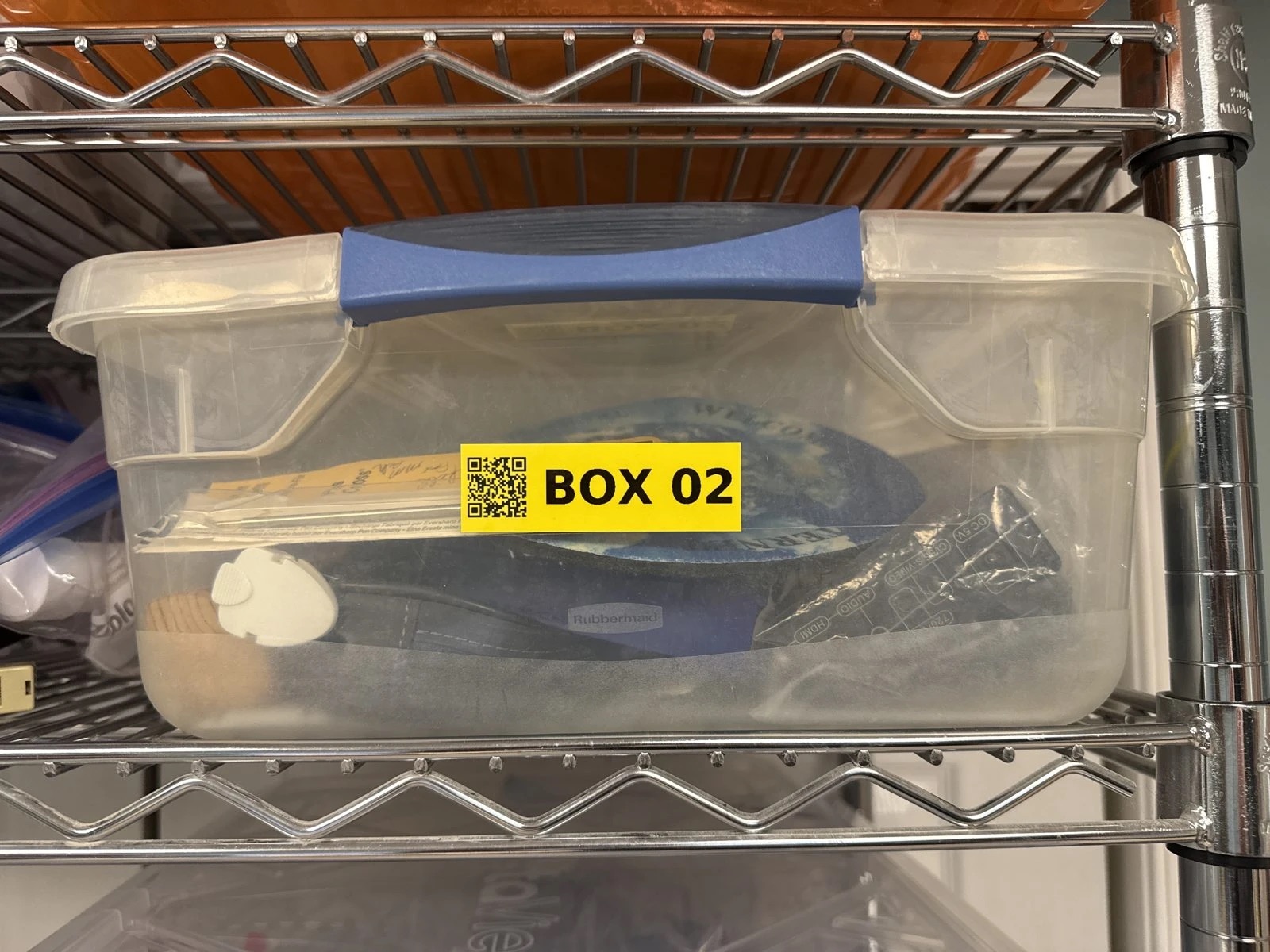 A clear tote on a wire shelf with a yellow BOX 02 label and QR code